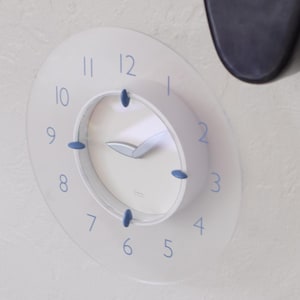 May include: A white clock with blue numbers and hands. The clock has a white face with a silver rim and blue accents.