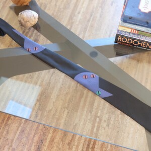 May include: A black tie with a blue and pink geometric pattern. The tie is lying on a glass table.
