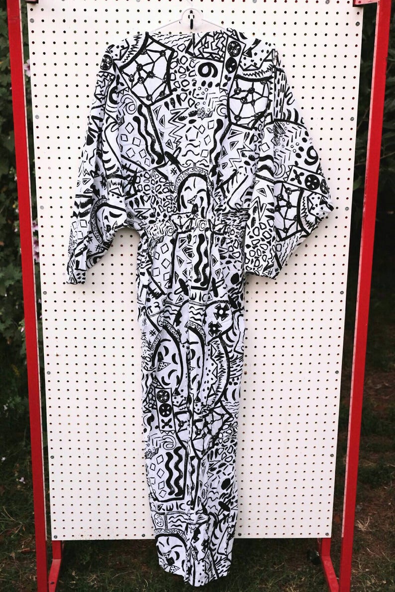 May include: A white jumpsuit with a black and white abstract pattern. The pattern includes geometric shapes, lines, and swirls.