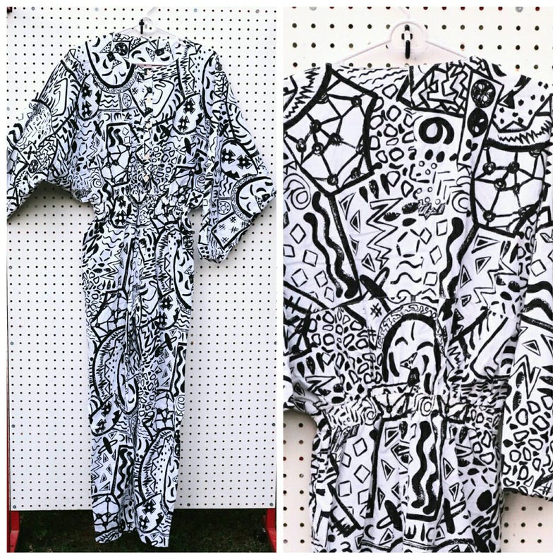 May include: A black and white jumpsuit with a geometric pattern. The jumpsuit has a wide, flowing sleeve and a cinched waist.