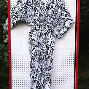 May include: A white jumpsuit with a black and white abstract pattern. The jumpsuit has a button-up front and a wide leg.