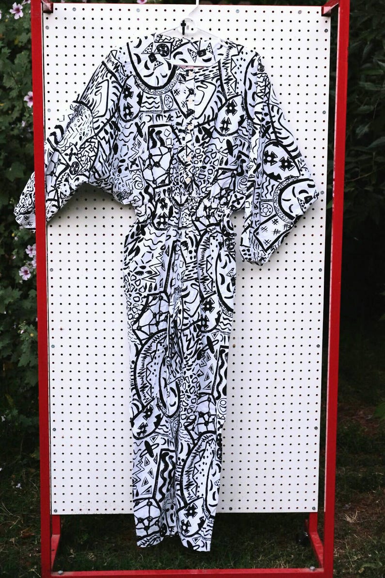 May include: A white jumpsuit with a black and white abstract pattern. The jumpsuit has a button-up front and a wide leg.