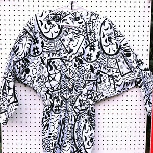 May include: A white and black patterned long-sleeved shirt with a button-up front. The shirt has a geometric and abstract design.