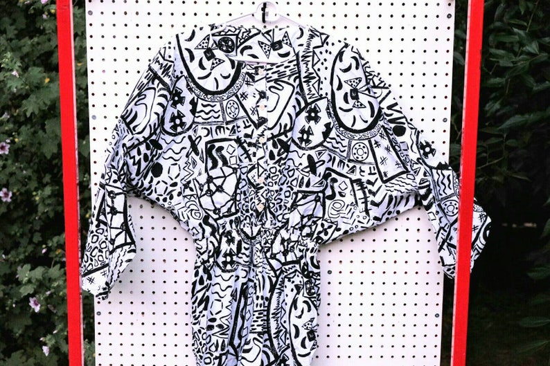 May include: A white and black patterned long-sleeved shirt with a button-up front. The shirt has a geometric and abstract design.