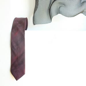 May include: A burgundy patterned necktie hanging on a white wall.