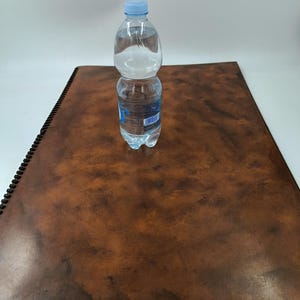 Puede incluir: Una botella de agua de plástico transparente con una tapa azul se encuentra sobre una superficie de cuero marrón.