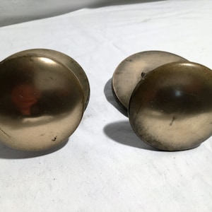 May include: Two round, brass-colored door knobs with a smooth, shiny finish.