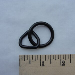 Puede incluir: Anillo de metal negro con un bucle triangular. El anillo tiene un diámetro de aproximadamente 2,5 cm.