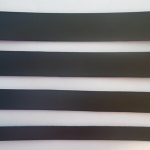 May include: Four strips of black leather, each with a different width, are laid out horizontally on a white surface.