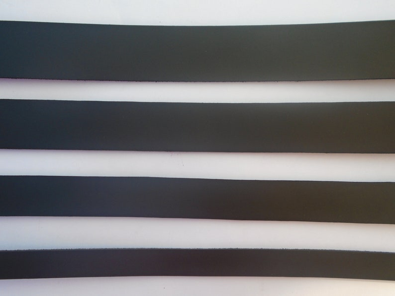 May include: Four strips of black leather, each with a different width, are laid out horizontally on a white surface.