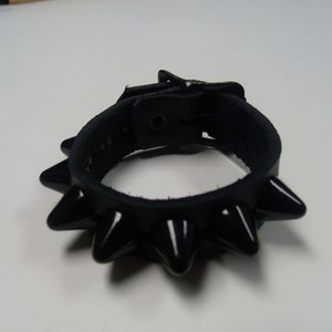 May include: A black leather bracelet with a buckle closure and a row of black spikes around the edge.