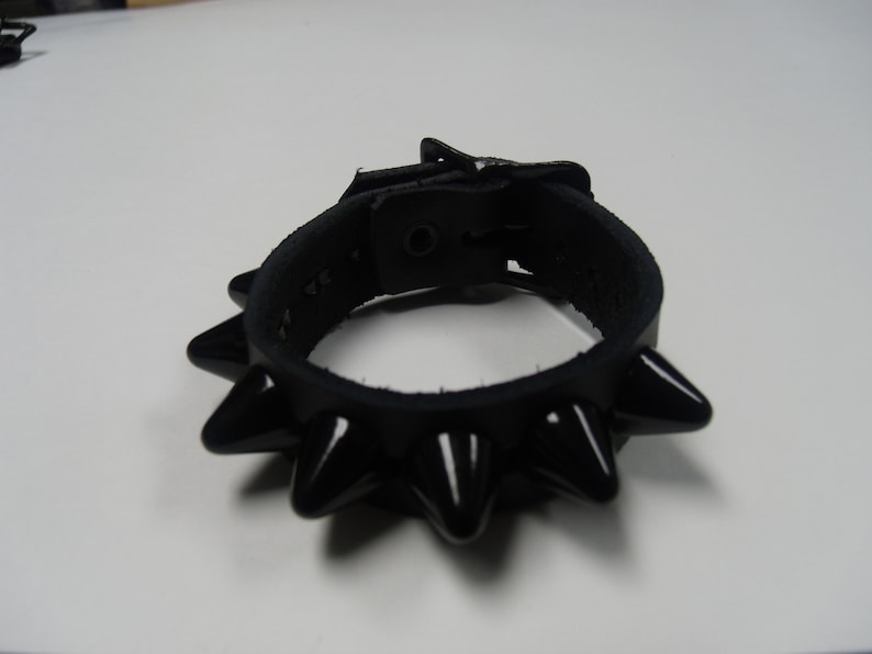 May include: A black leather bracelet with a buckle closure and a row of black spikes around the edge.