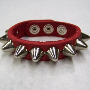 May include: Red leather bracelet with silver metal spikes. The bracelet has three adjustable holes.