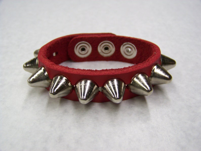 May include: Red leather bracelet with silver metal spikes. The bracelet has three adjustable holes.