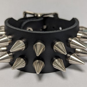 May include: A black leather bracelet with silver metal spikes. The bracelet has a buckle fastening.