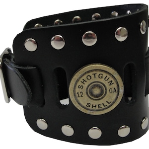 May include: Black leather bracelet with silver studs and a shotgun shell charm. The charm has the words "SHOTGUN SHELL 12 GA" engraved on it.