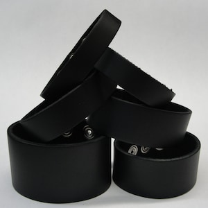May include: A stack of five black leather bracelets with silver metal accents. The bracelets are stacked in a triangular shape.