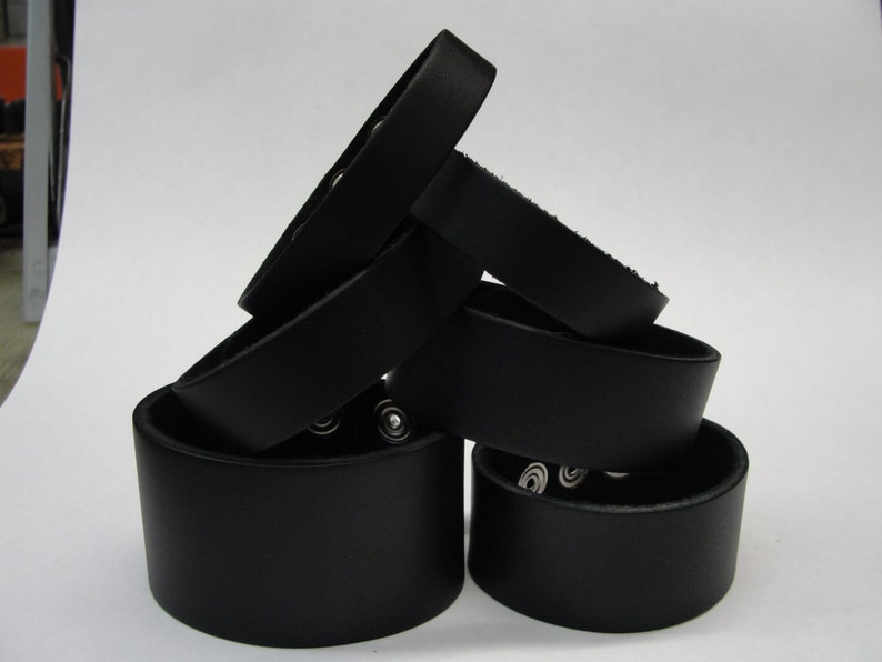 May include: A stack of five black leather bracelets with silver metal accents. The bracelets are stacked in a triangular shape.