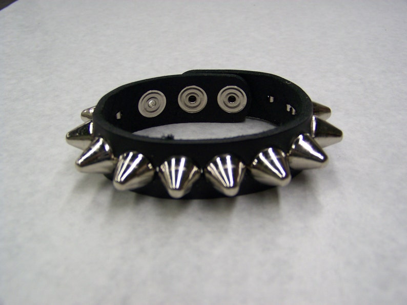 May include: Black leather bracelet with silver metal spikes. The bracelet has three snap closures.