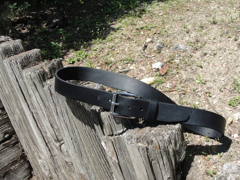 May include: A black leather belt with a silver buckle. The belt is lying on a wooden surface.