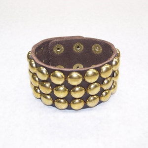 May include: A brown leather bracelet with three rows of gold-toned metal studs.