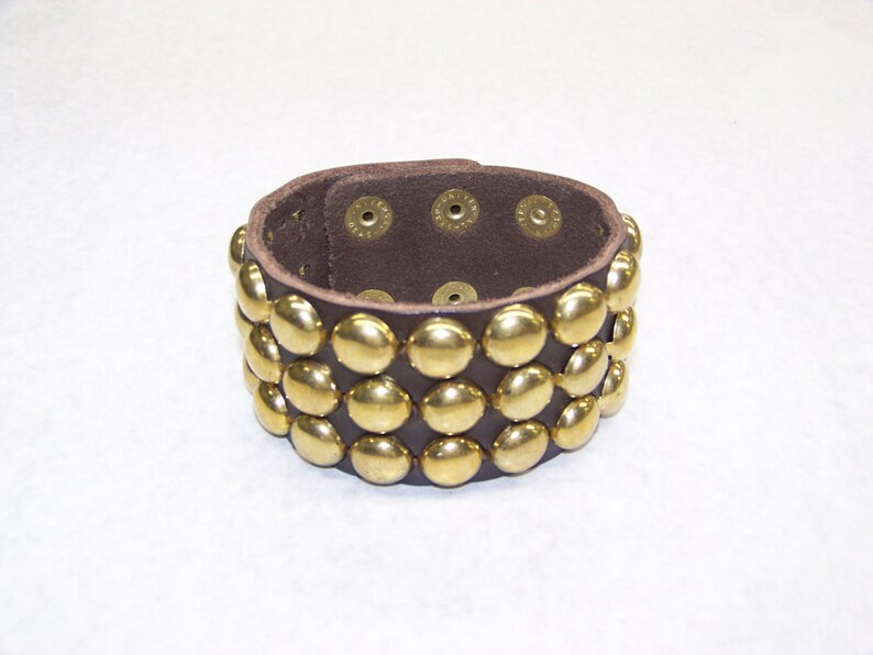 May include: A brown leather bracelet with three rows of gold-toned metal studs.