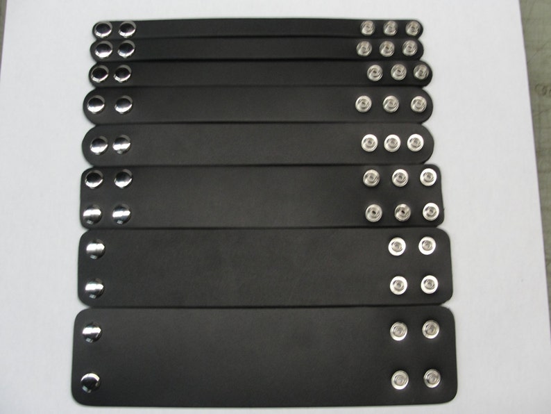 May include: A set of eight black leather bracelets with silver metal studs. Each bracelet has a different number of studs.