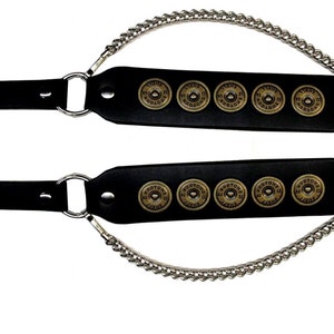 May include: A pair of black leather guitar straps with a silver chain and five gold-coloured bullet casings on each strap.