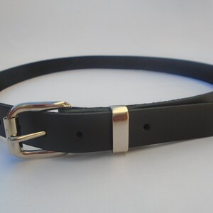 May include: A black leather belt with a silver buckle. The belt is approximately 2.5 cm wide and has a pointed end.