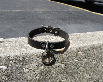 May include: Black leather choker with a silver ring and metal hardware. The choker has the text "GEN 970" embossed on it.