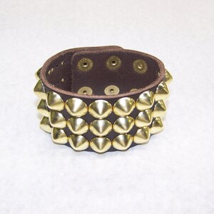 May include: A brown leather bracelet with three rows of gold pyramid-shaped studs.