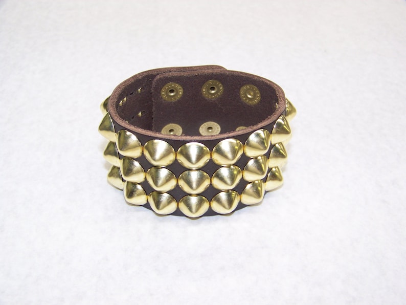 May include: A brown leather bracelet with three rows of gold pyramid-shaped studs.