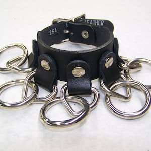 May include: Black leather choker with a silver buckle and six silver rings attached. The choker is labelled "U.S. LEATHER 264".