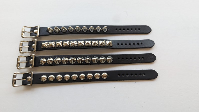 May include: Four black leather bracelets with silver studs. The bracelets have different styles of studs, including pyramid, square, and round.