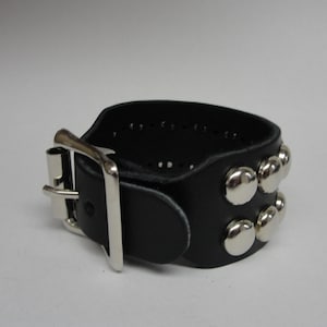 May include: A black leather bracelet with a silver buckle and silver studs. The bracelet is adjustable.