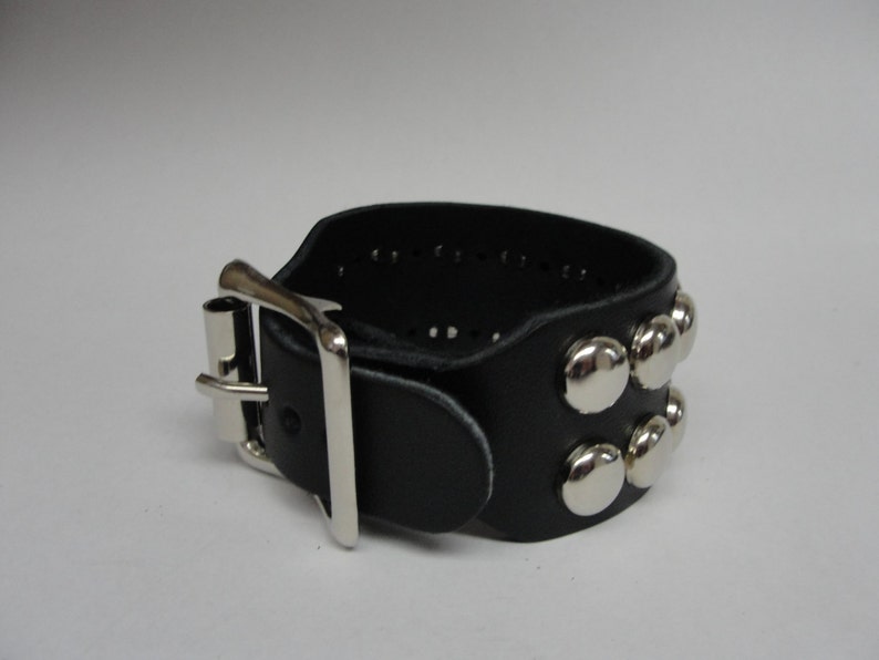 May include: A black leather bracelet with a silver buckle and silver studs. The bracelet is adjustable.