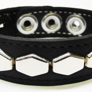 May include: Black leather bracelet with silver hexagonal studs and three snap closures.