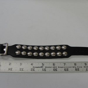 May include: A black leather bracelet with silver metal studs. The bracelet has a buckle closure and is approximately 7 inches long.