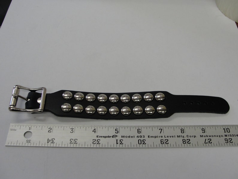 May include: A black leather bracelet with silver metal studs. The bracelet has a buckle closure and is approximately 7 inches long.