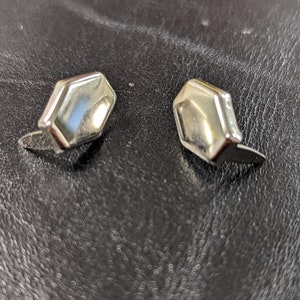 May include: A pair of silver-toned metal stud earrings, each featuring a smooth, polished, hexagonal-shaped face with beveled edges. The earrings have a reflective surface and are designed with a post backing for secure attachment to the earlobe.