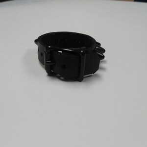 May include: A black leather bracelet with a buckle closure and metal spikes.