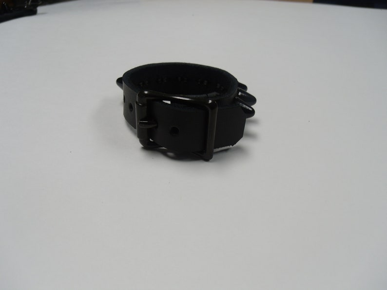May include: A black leather bracelet with a buckle closure and metal spikes.