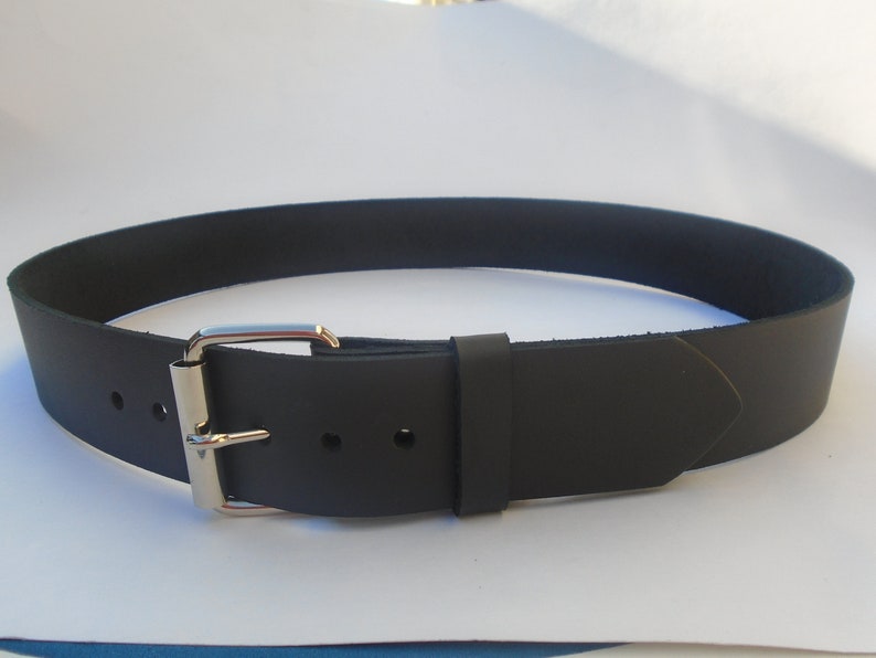 May include: A black leather belt with a silver buckle. The belt is approximately 3.8 cm wide and has a pointed end.