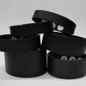 May include: A stack of six black leather bracelets with silver snap closures.