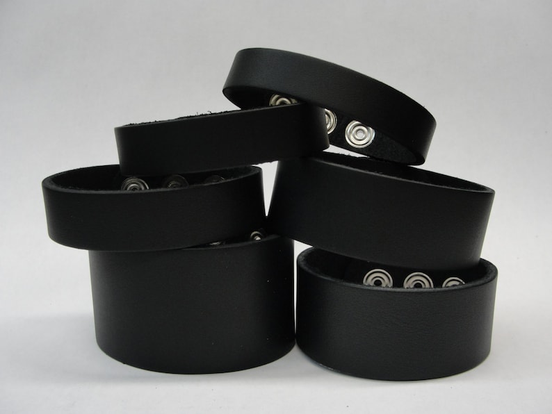 May include: A stack of six black leather bracelets with silver snap closures.