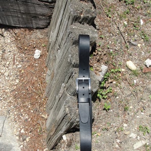 May include: A black leather belt with a silver buckle. The belt is lying on a wooden surface.