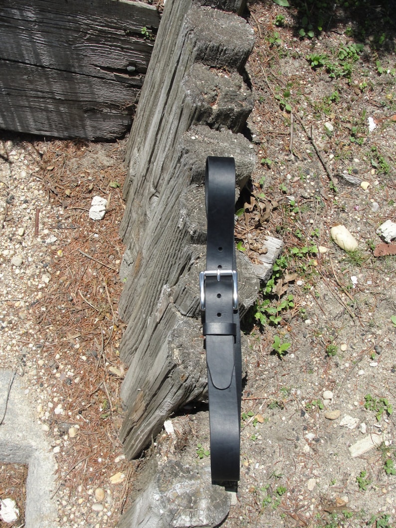 May include: A black leather belt with a silver buckle. The belt is lying on a wooden surface.