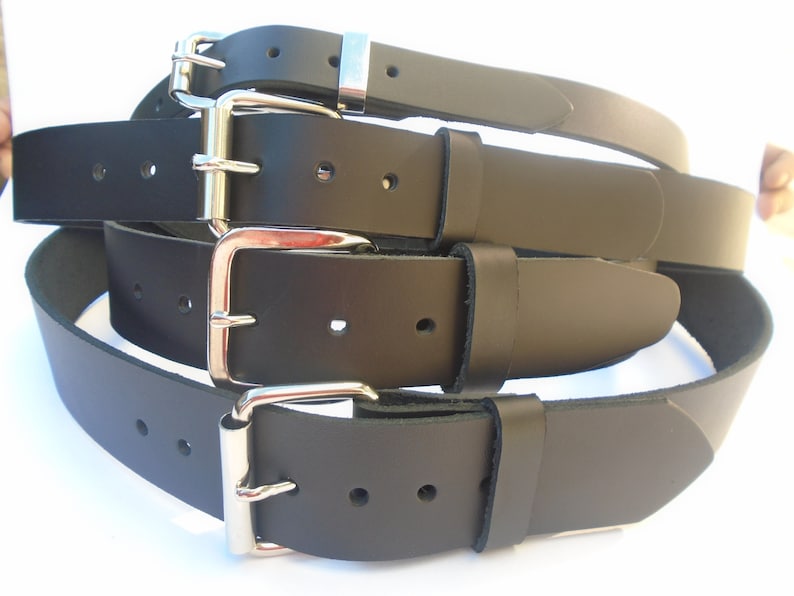 May include: Four black leather belts with silver buckles. The belts are stacked on top of each other.