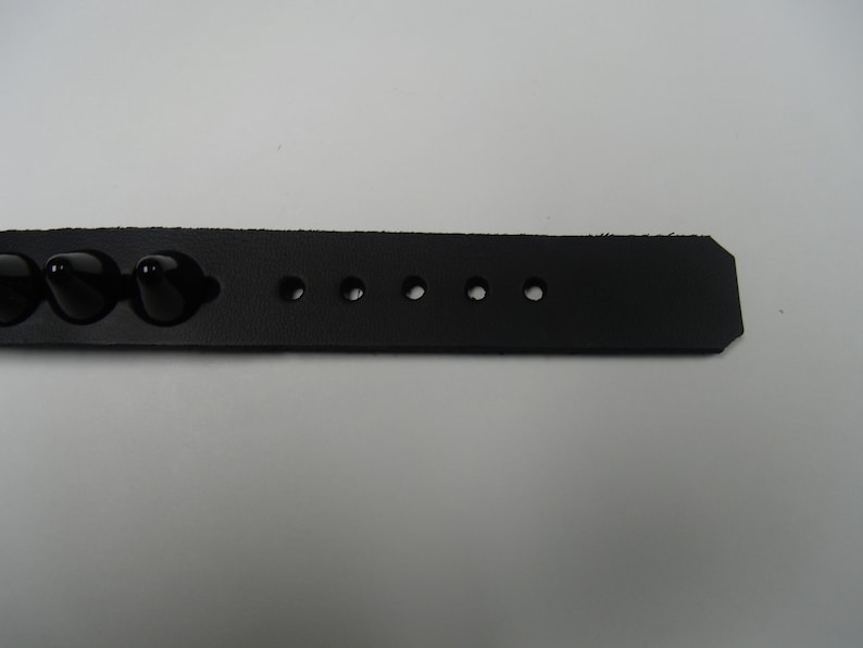 May include: Black leather bracelet with black studs and multiple holes for adjusting the size.