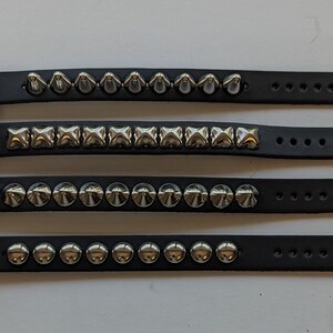 May include: Four black leather bracelets with silver studs. The bracelets have different styles of studs, including pyramid, square, and round.
